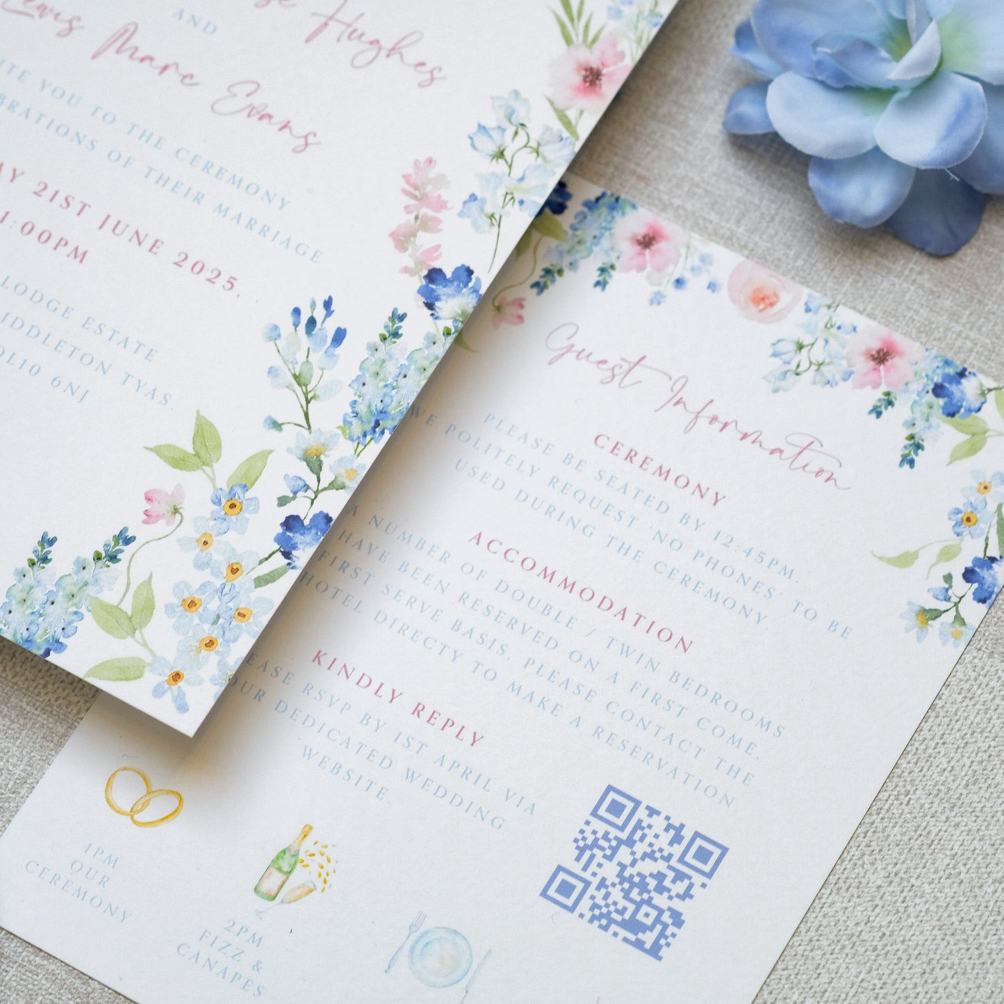Watercolour, painterly-style wedding invitations with blue and pink wildflower decorations with information on the ceremony and wedding accommodation