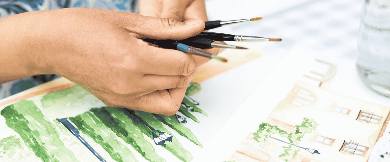 hand holding brushes with illustration of cypress trees in background