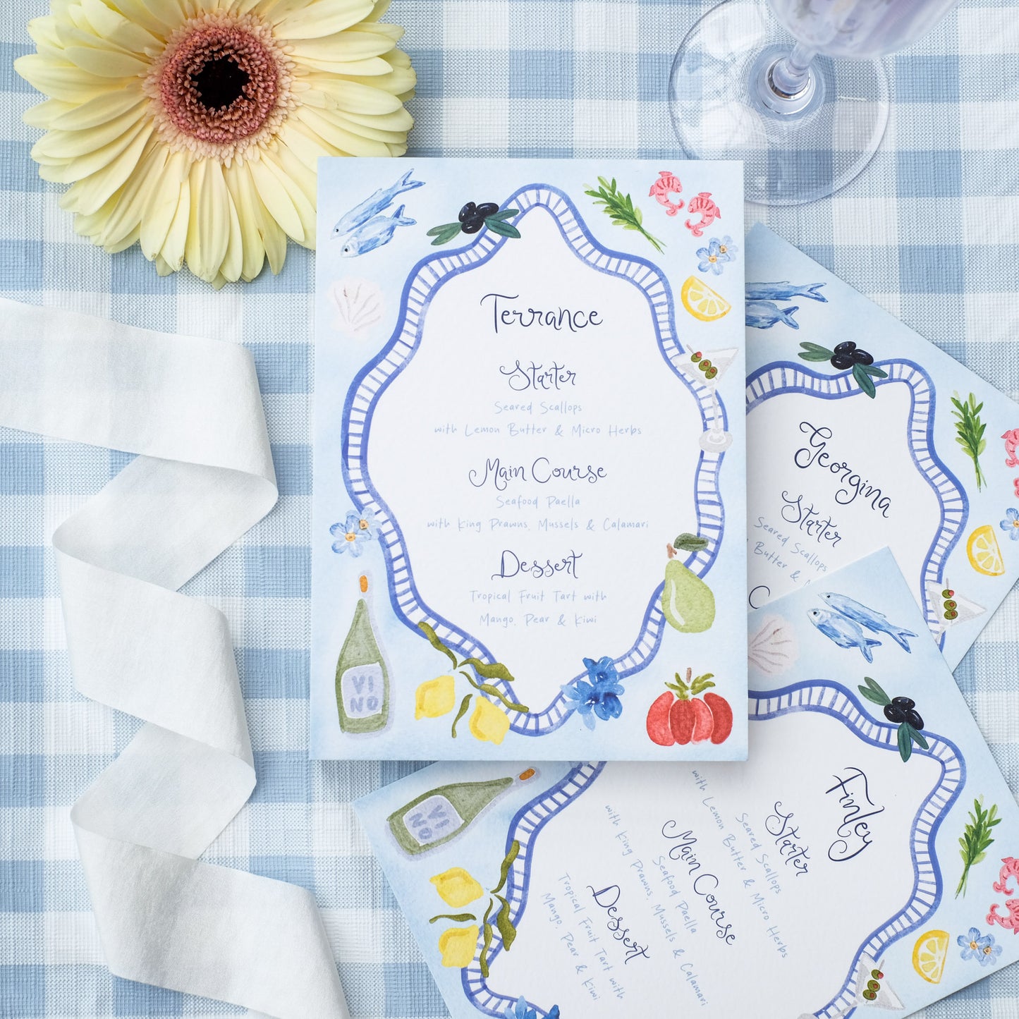 Hand painted wedding menu with blue border and watercolour illustrations of lemons, fish, shrimps and olives
