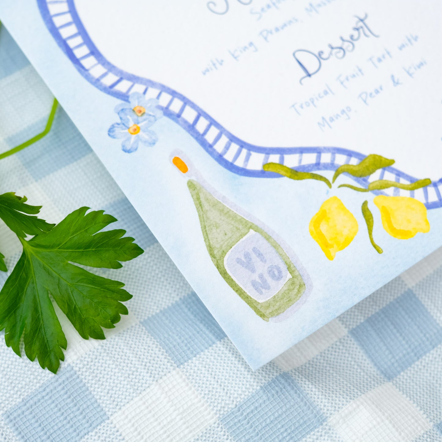 Hand painted wedding menu with blue border and watercolour illustrations of lemons, fish, shrimps and olives
